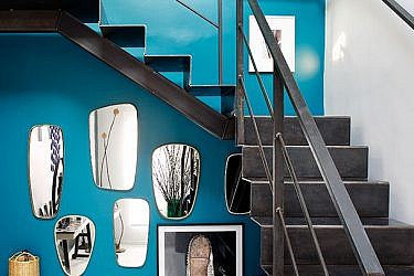 בכניסה המרשימה לבית שולבו מגוון אלמנטים הלוכדים את תשומת הלב של הבאים, בהם מדרגות מתכת, קיר בגון טורקיז ואוסף מראות וינטג' | צילום: Francis Amiand