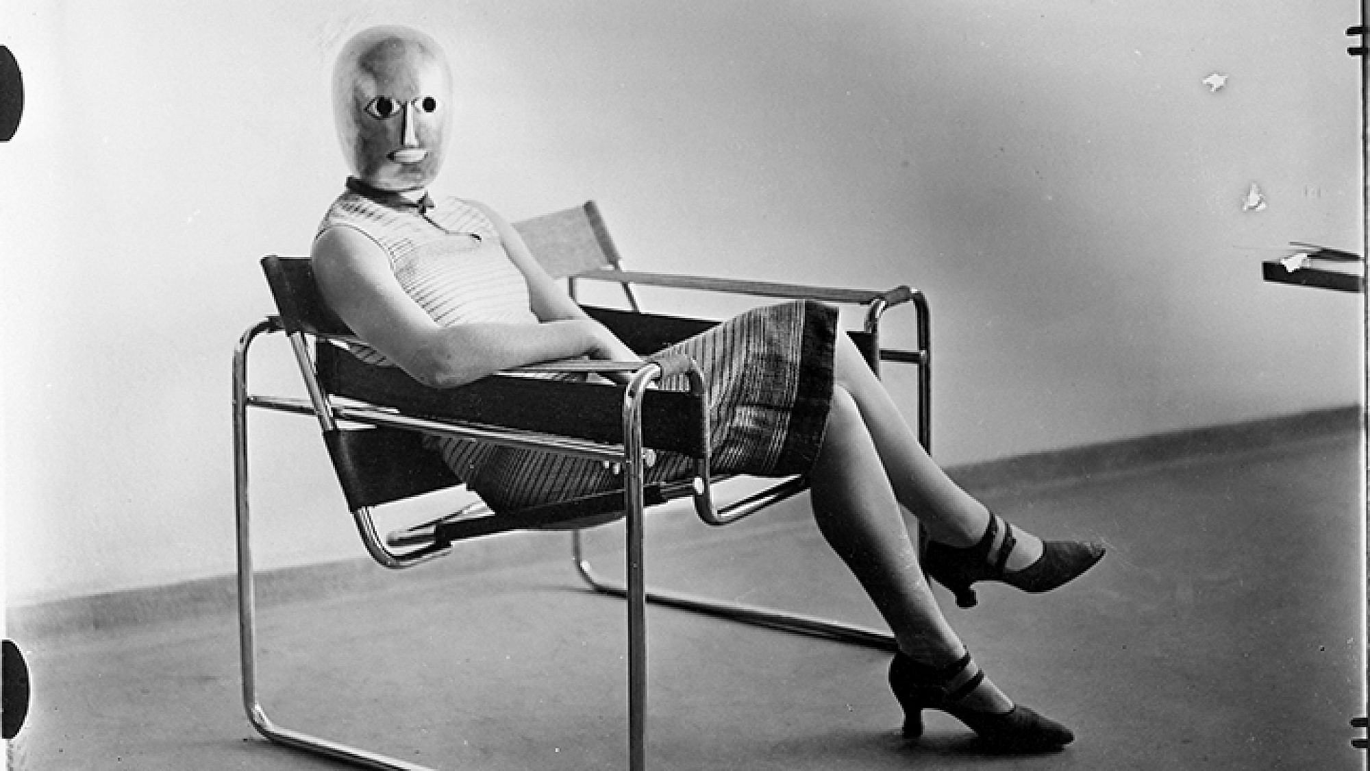 אריך קונסמולר, אשה יושבת על כיסא וסילי בעיצוב מרסל ברוייר, ועל פניה מסכה של אוסקר שלמר, 1926 בקירוב, תצלום שחור-לבן | ארכיון באוהאוס, ברלין