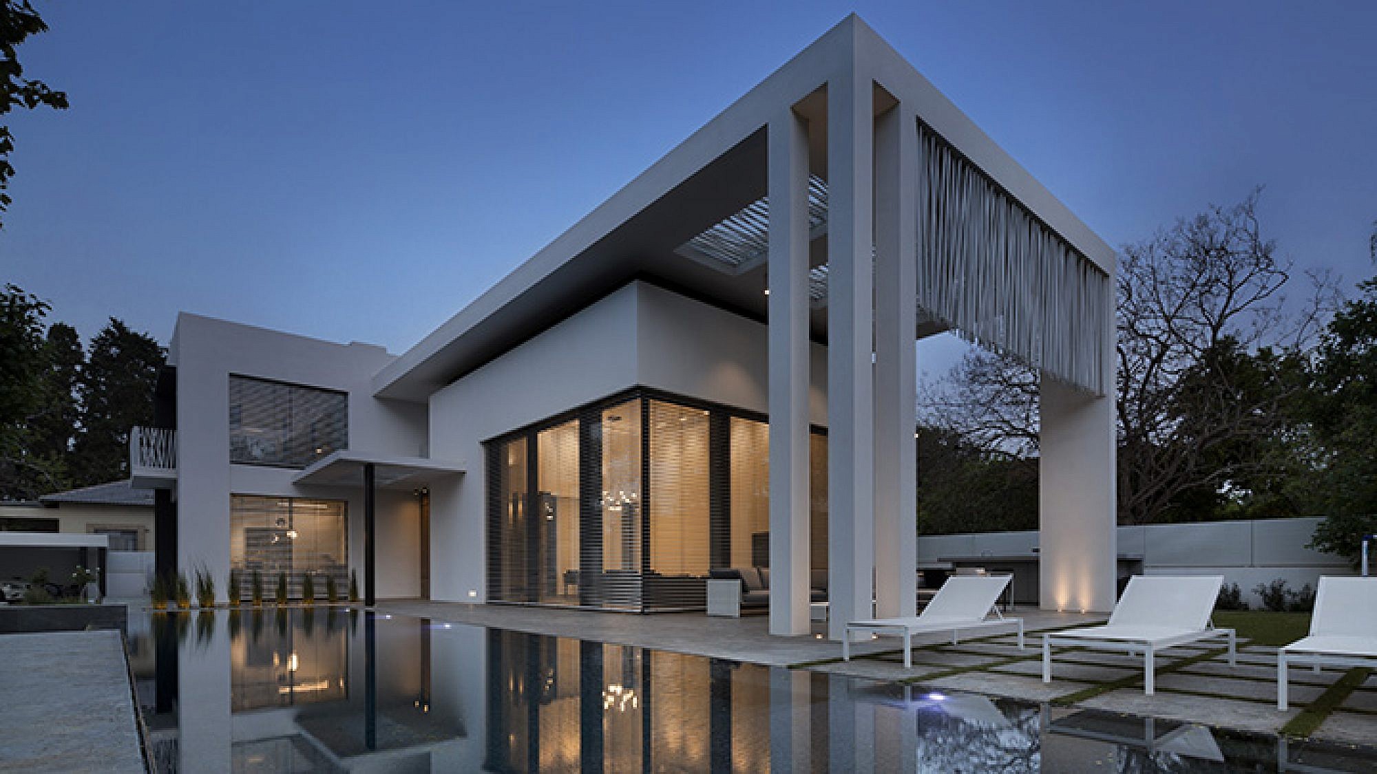 בית גדול בעיצוב נקי: חזיתות לבנות ועמודים ישרים עם מסך הצללה פיסולי ממוטות פלדה שמוסיף עניין | צילום: אסף פינצ'וק