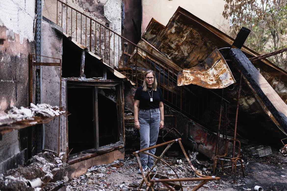 "לעולם לא נשכח". מירי גד-מסיקה על רקע ביתה ההרוס בקיבוץ בארי | צילום: מאיה אשל