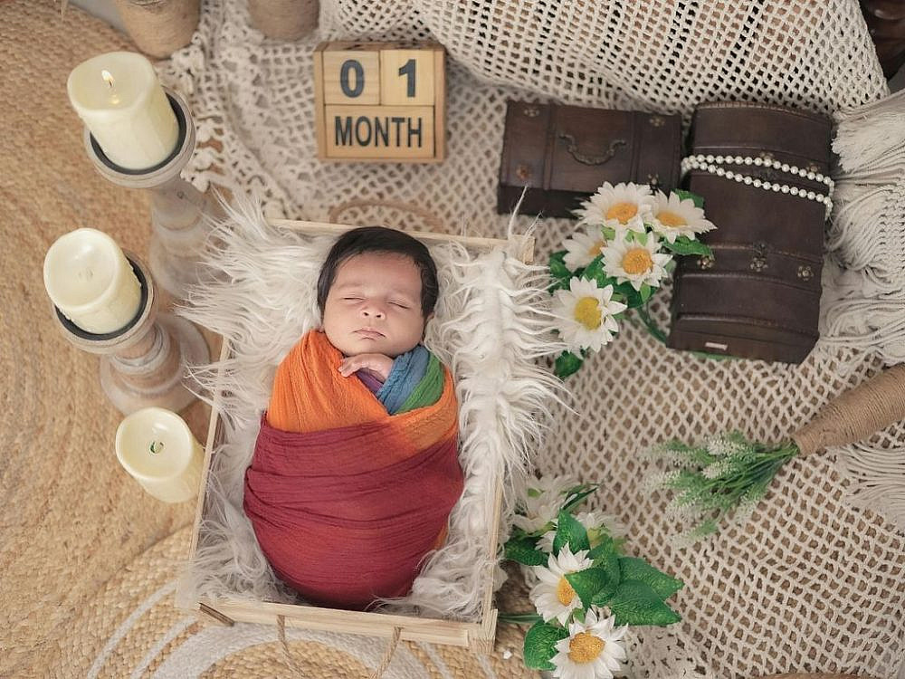 תינוק בן חודש שוכב עטוף עם סימן של חודש אחד לידו. צילום: Canva